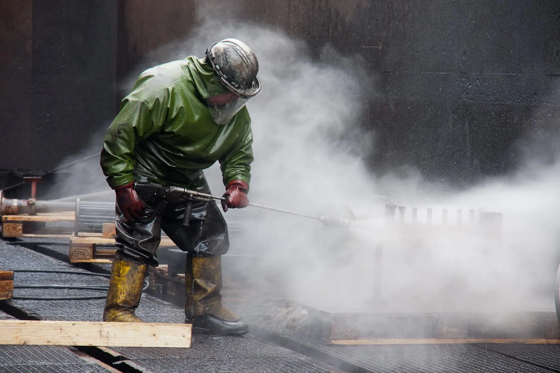 A worker wearing effective PPE when using a pressure washer for dumpster pad cleaning.