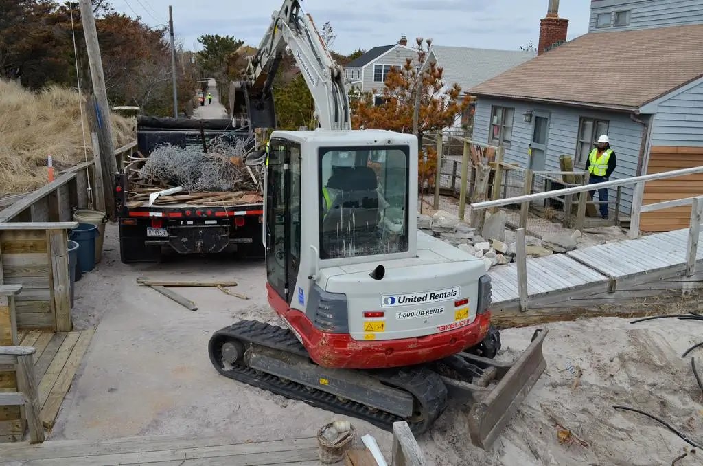 Cleanup workers using a backhoe to clear storm debris. In some cases, this special equipment will raise junk removal costs in Kentucky.