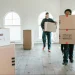 Two junk removal workers carrying boxes of unwanted items out of an apartment.